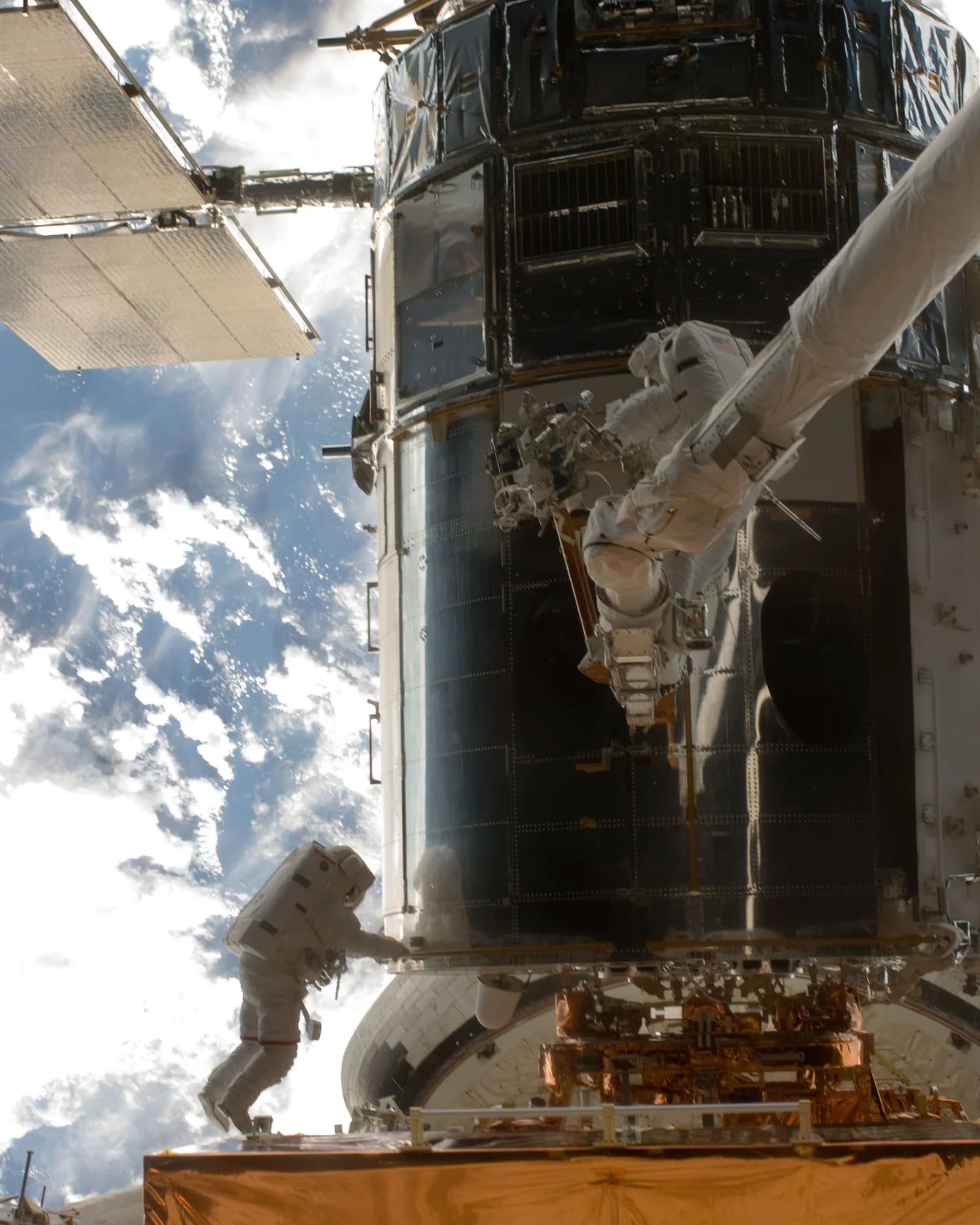 Zwei Astronauten arbeiten gemeinsam beim Außeneinsatz am Hubble-Teleskop, Erde im Hintergrund